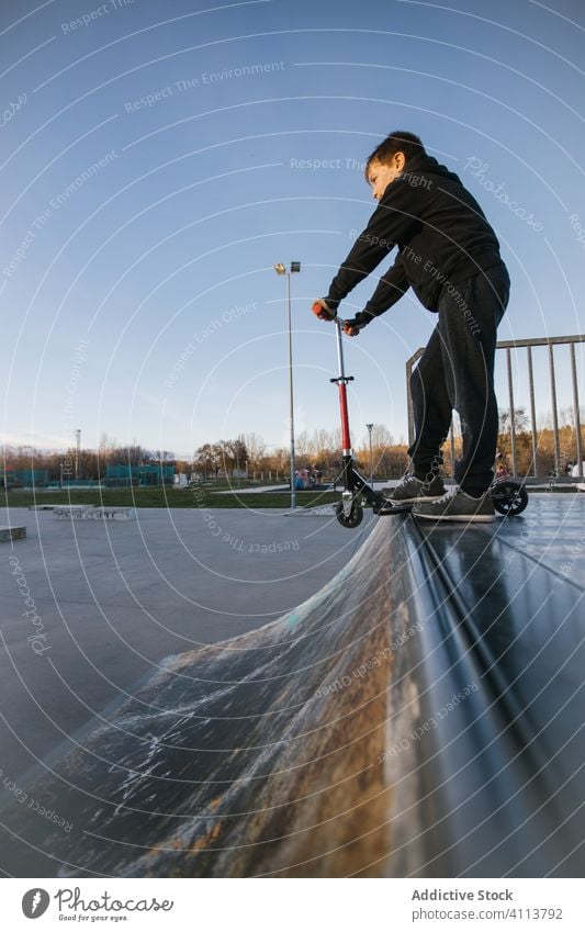 Junge fährt Roller auf einer Rampe im Park Skateplatz Tretroller extrem Sport urban aktiv üben Mitfahrgelegenheit Kick Teenager Trick Skateboard männlich Stunt