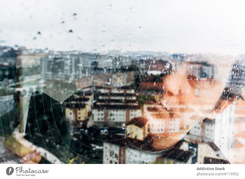 Depressiver Mann schaut durchs Fenster traurig Depression Isolation Coronavirus heimwärts verzweifelt einsam unglücklich jung männlich nass Regen Melancholie