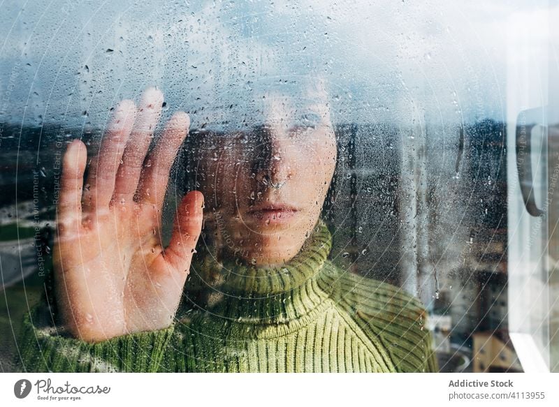 Melancholische junge Frau schaut durchs Fenster traurig Depression Isolation Coronavirus heimwärts verzweifelt einsam unglücklich männlich nass Regen