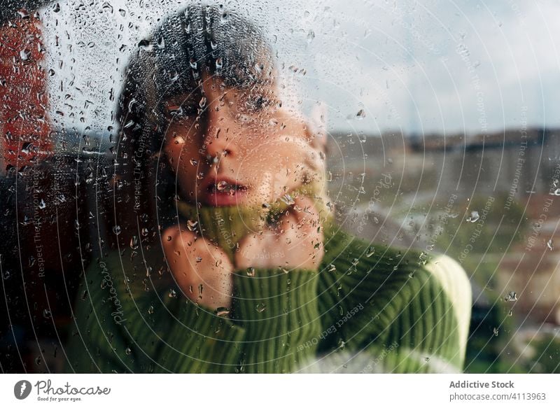 Melancholische junge Frau schaut durchs Fenster traurig Depression Isolation Coronavirus heimwärts verzweifelt einsam unglücklich männlich nass Regen