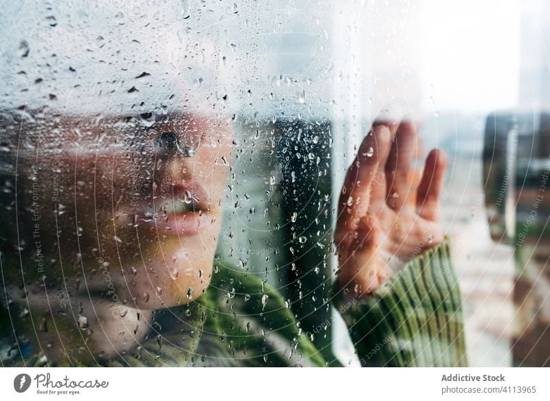 Melancholische junge Frau schaut durchs Fenster traurig Depression Isolation Coronavirus heimwärts verzweifelt einsam unglücklich männlich nass Regen