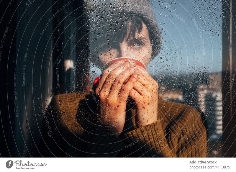 Nachdenkliche Frau trinkt Kaffee am Fenster traurig Depression trinken Selbstisolierung heimwärts unglücklich einsam COVID19 Melancholie jung nass Regen