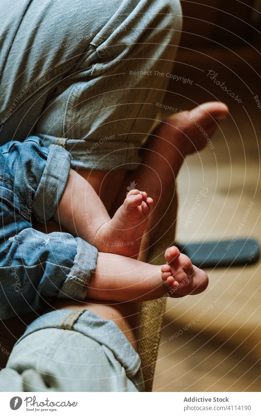 Crop-Mutter mit Baby sitzt am Fenster heimwärts ruhen Umarmung Angebot Liebe Frau Pflege Barfuß Jeanshose Stuhl Raum gemütlich Kind lässig Wochenende Windstille