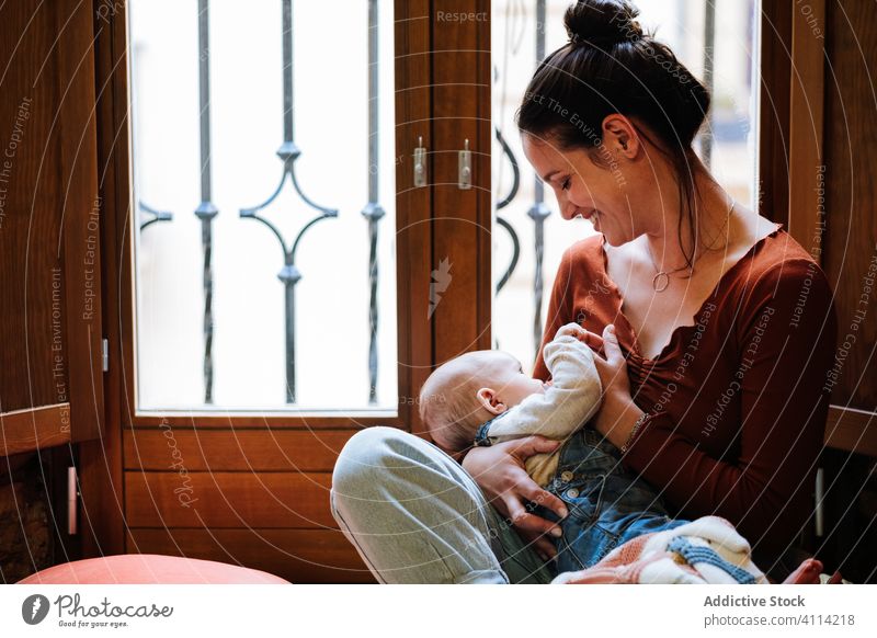 Glückliche Mutter stillt Baby am Fenster Futter Brust heimwärts Liebe ruhen gemütlich sitzen heiter Frau niedlich Raum Umarmung Umarmen Lächeln Kind Kindheit