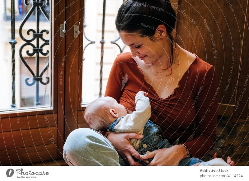 Glückliche Mutter stillt Baby am Fenster Stillen Futter Brust heimwärts Liebe ruhen gemütlich sitzen Frau niedlich Raum Umarmung Umarmen Lächeln Kind Kindheit