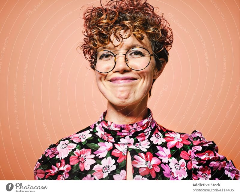 Positiv gestylte Frau mit Brille Glück Stil trendy jung Lächeln heiter Mode geblümt Freude attraktiv elegant positiv Model hübsch froh Outfit krause Haare