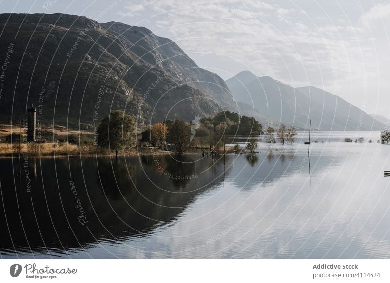 Ruhiger See, in dem sich felsige Berge spiegeln Berge u. Gebirge Reflexion & Spiegelung sonnig Landschaft Felsen Hochland Cloud Baum Windstille ruhig Wasser