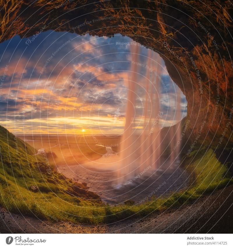 Höhle mit Wasserfall bei Sonnenuntergang MEER Ufer Eingang wolkig Himmel Island Abend majestätisch Gras Stein Kaskade Moos Meer Landschaft Natur rau platschen