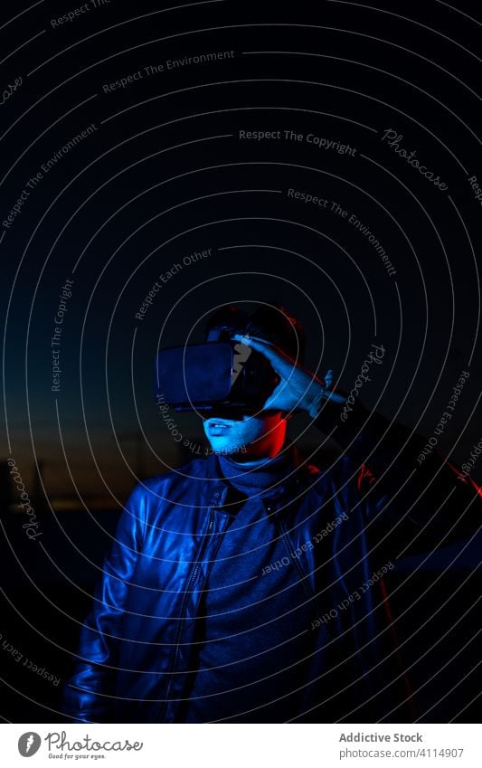 Junger Mann erforscht virtuelle Realität Nacht VR dunkel Straße Headset Schutzbrille futuristisch leuchten neonfarbig rot Licht männlich modern Gerät Apparatur