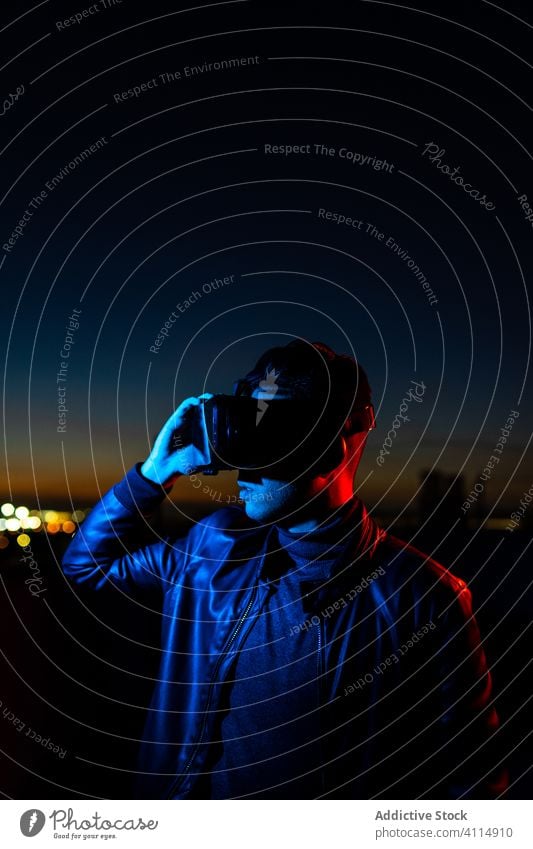 Junger Mann erforscht virtuelle Realität Nacht VR dunkel Straße Headset Schutzbrille futuristisch leuchten neonfarbig rot Licht männlich modern Gerät Apparatur