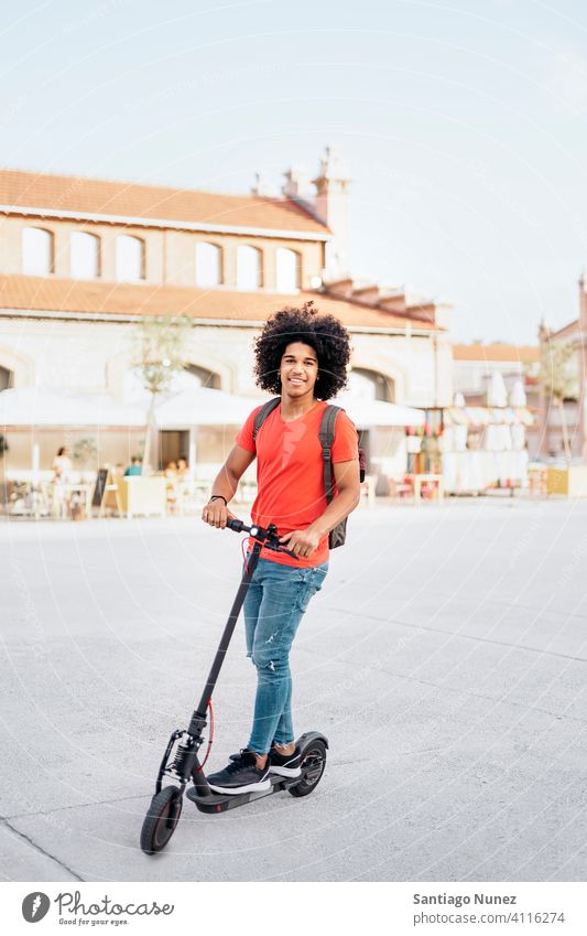 Glücklicher afroamerikanischer Junge, der einen elektrischen Motorroller fährt Vorderansicht in die Kamera schauen Afro-Look jung Mann schwarz Afroamerikaner