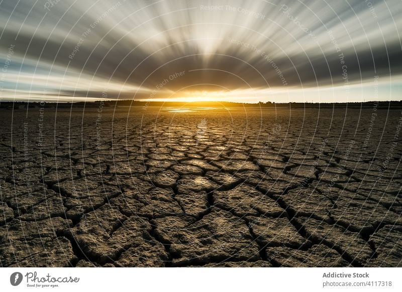 Trockenes rissiges Gelände unter bewölktem Sonnenuntergangshimmel Dürre trocknen Boden Natur wüst Land Riss heiß Ökologie flau Himmel Hintergrund Textur