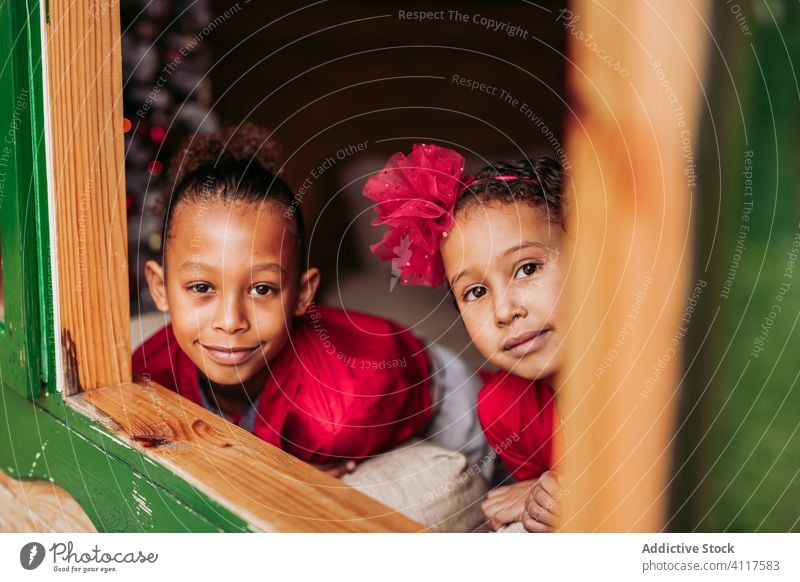 Fröhliche ethnische Kinder schauen aus dem Fenster Haus Glück Geschwisterkind Zusammensein heiter hölzern ländlich Lächeln heimwärts Lifestyle Landschaft Freude