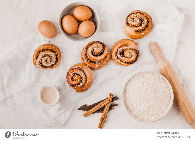 Süße Brötchen und Zutaten auf weißem Tisch Zimt rollen süß backen Bestandteil kleben Mehl Gewürz Zucker Küche Dessert Teigwaren lecker Zusammensetzung Kulisse