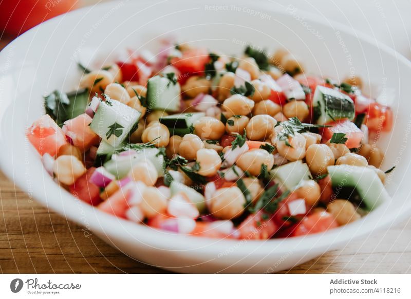 Schüssel mit Gemüsesalat und Kichererbsen Salatbeilage Schalen & Schüsseln Gesundheit Veganer Silberwaren Tomate Salatgurke Petersilie Holz Tisch Gabel Messer