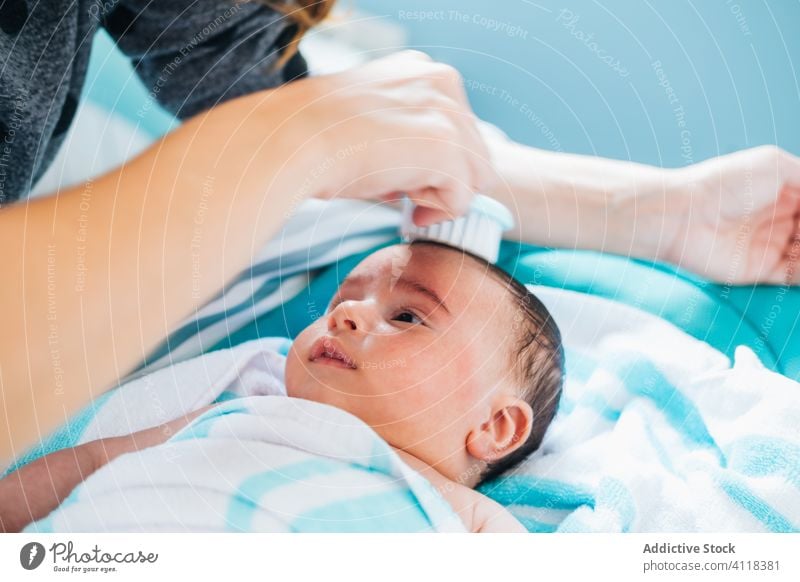 Crop Mutter Kämmen Baby in blauen Kinderzimmer Frau Kamm neugeboren sanft Bad Lügen rein Pflege Decke dunkles Haar Liebe niedlich Eltern ethnisch Kindheit