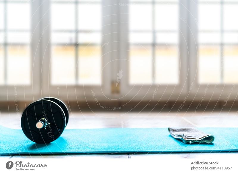 Handtuch und zusammenklappbare Hantel auf Sportmatte in leichtem Trainingsraum Unterlage Kurzhantel Fitness Wellness Gerät Fitnessstudio vorbereiten Metall