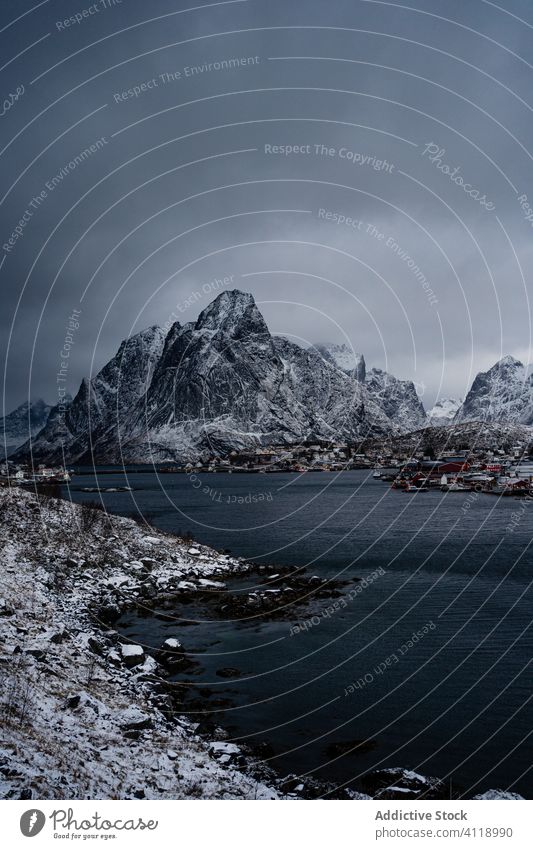 Malerische Landschaft mit Küstenstadt am Fuße der schneebedeckten Felsen unter grauem, bewölktem Himmel hafen Berge u. Gebirge Schnee Natur Wasser Hochland Kamm