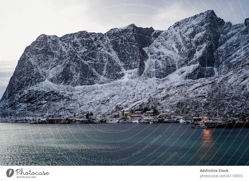 Malerische Landschaft mit Küstenstadt am Fuße der schneebedeckten Felsen unter grauem, bewölktem Himmel hafen Berge u. Gebirge Schnee Natur Wasser Hochland Kamm