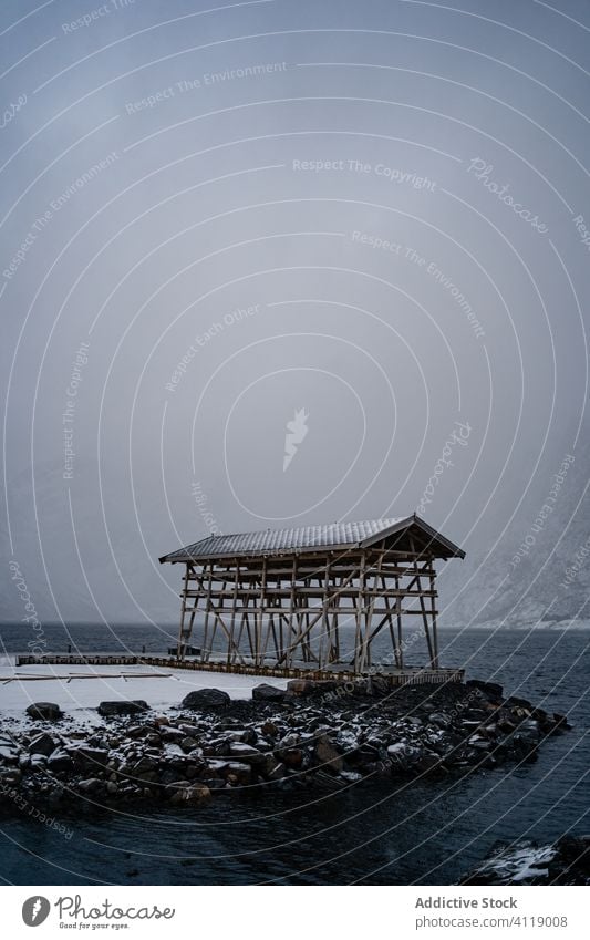 Hölzerne Konstruktion auf felsigen Ufer gegen nebligen Berg im Winter bewölkten Tag Berge u. Gebirge kalt Nebel Fjord Kamm Schnee hölzern hafen Wasser bedeckt