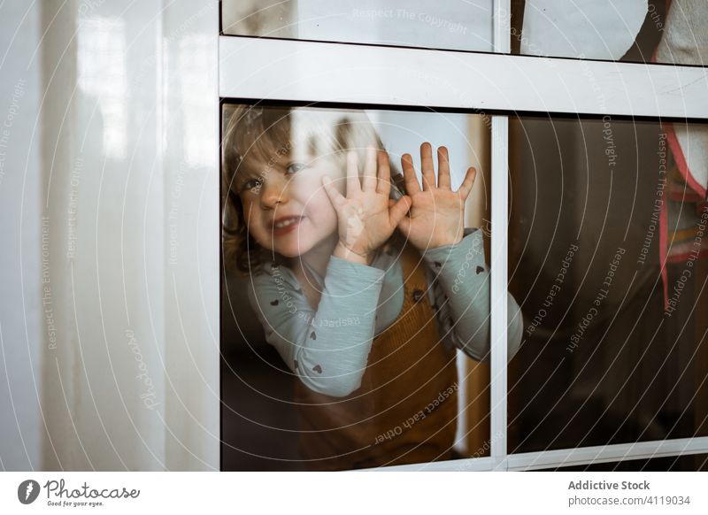 Glückliches kleines Mädchen hinter dem Fenster heimwärts Lächeln lässig niedlich wenig berühren Glas Kind heiter Kindheit Raum spielerisch neugierig ruhen