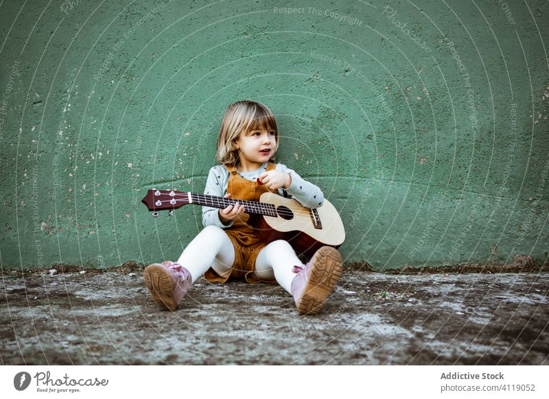 Mädchen mit Ukulele an schäbiger Wand sitzend Musik Kickroller spielen lässig wenig rau Boden verwittert grün Kind Straße Gebäude Grunge Instrument Klang Talent