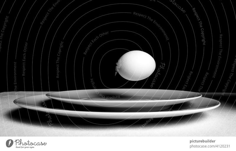 Weißes Ei schwebt über weißen Tellern vor schwarzem Hintergrund schwebend fliegend Frühstück Lebensmittel Ernährung Innenaufnahme Studioaufnahme