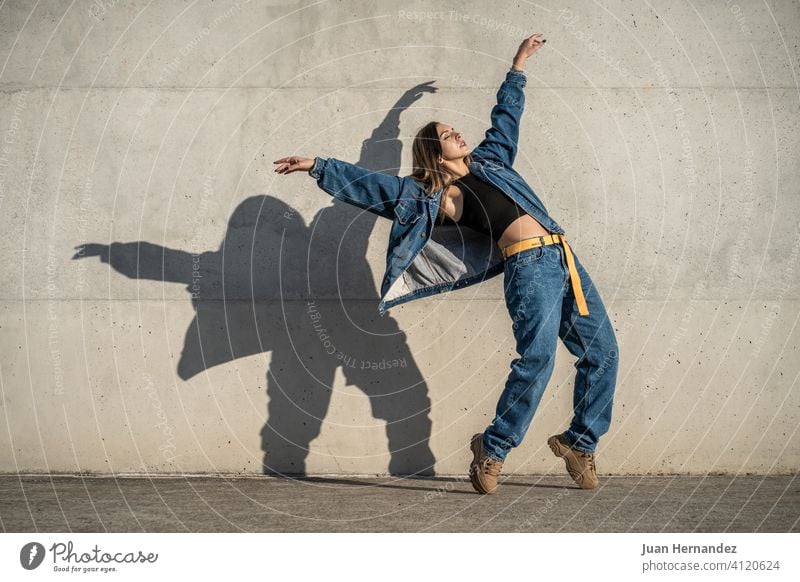 Tänzerin Frau macht eine Pose wie ein Adler. Casual Kleid und Schatten an der Wand reflektiert. mögen lässig Textfreiraum Kopierbereich copyspace Gleichgewicht