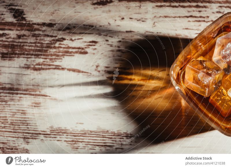 Glas Scotch in Strahlen auf alten rustikalen Tisch in der Dunkelheit Whiskey Bourbon Alkohol Getränk Eis trinken liquide Schnaps Cognac Weinbrand durchsichtig