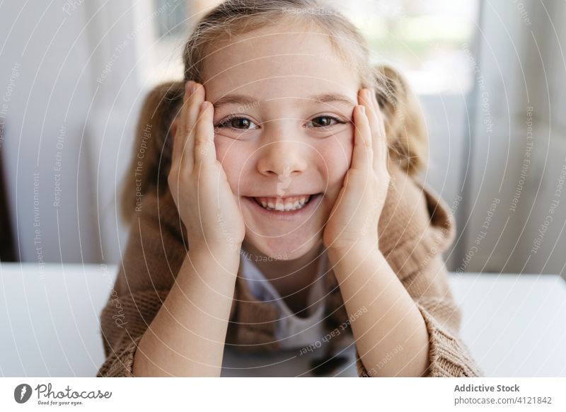 Glückliches kleines Mädchen schaut in die Kamera in einem gemütlichen Haus Lächeln heimwärts Kindergarten sich auf die Hand lehnen charmant Porträt niedlich