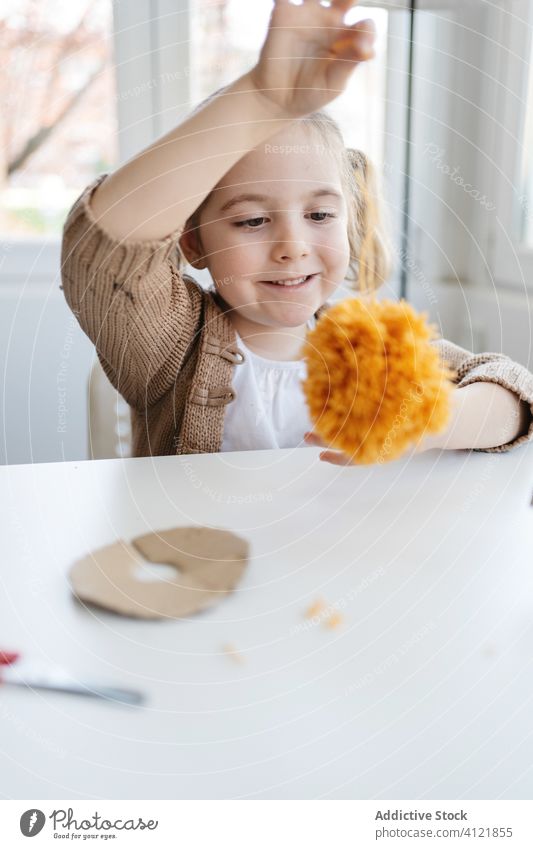 Fröhliches kleines Kind, das mit weichem Kunsthandwerk im hellen Haus spielt heiter Mädchen Pompom Glück spielen Basteln handgefertigt heimwärts Pompons