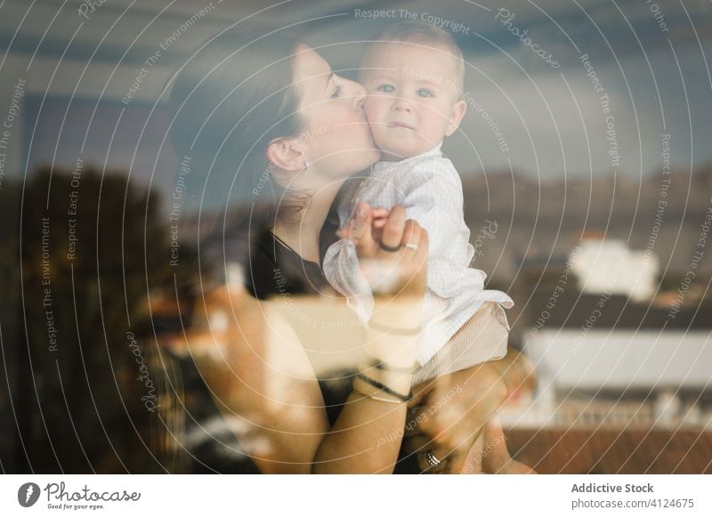 Liebevolle Mutter, die ihr Baby umarmt und küsst Kuss Umarmung Zusammensein niedlich Kleinkind Umarmen heimwärts Inhalt Outfit Fenster lässig Glück Kind Eltern