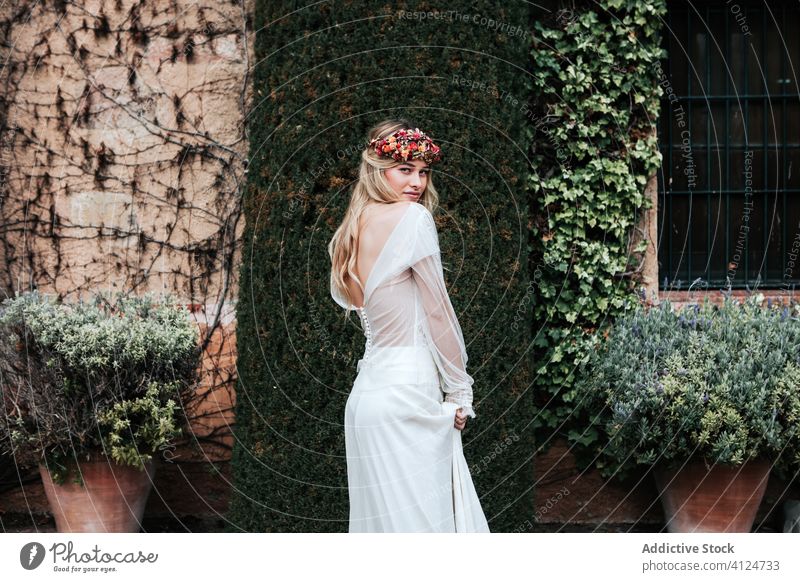 Junge Braut steht neben altem Anwesen Frau Haus Hof Buchse Wein Flora elegant Hochzeit jung Kleid Totenkranz gealtert eingetopft Blume Stil feiern Gelassenheit