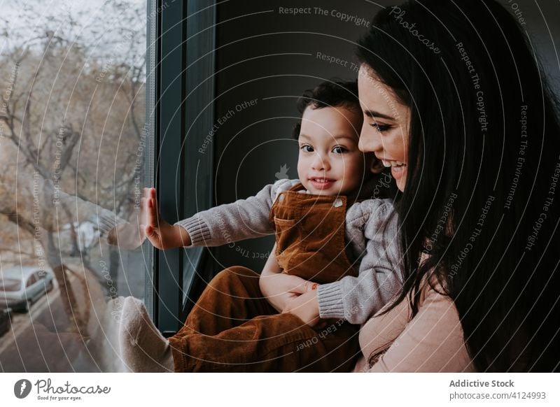 Positive junge Mutter und kleiner Sohn stehen am Fenster und bewundern die Aussicht heimwärts neugierig erkunden Punkt Ansicht Inhalt aufgeregt niedlich wenig