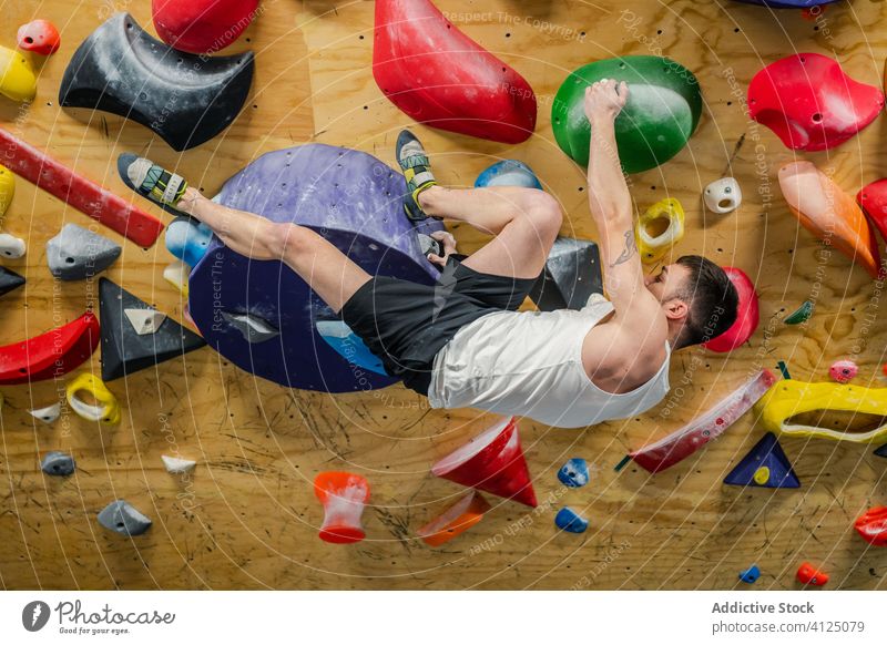 Starker Mann hängt an der Wand und übt Klettern Aufstieg Sport Training Felsbrocken Hobby Gerät Fitnessstudio Aktivität Athlet extrem männlich stark Übung