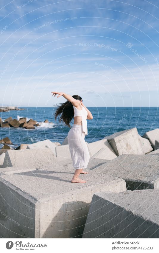 Moderne Frau steht auf Betonblock des Wellenbrechers MEER Tanzen sinnlich Kraft Harmonie Küste Zeitgenosse Konzept Stein Konstruktion Energie physisch jung Pose