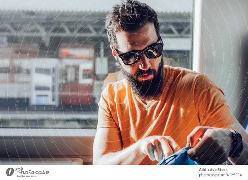 Mann mit Bart reist mit dem Zug Ausflug reisen Tasche träumen besinnlich Fenster Sonnenlicht Sommer ernst Verkehr Passagier Sitz Vollbart allein nachdenklich