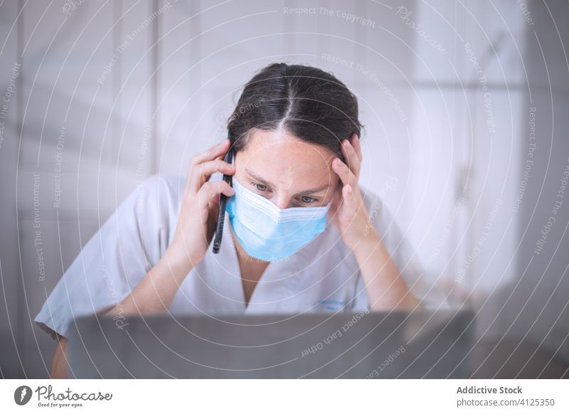 Junge Ärztin mit medizinischer Maske arbeitet am Laptop in der Klinik Frau Arzt Uniform Mundschutz Handschuh Schreibtisch ernst Krankenhaus professionell