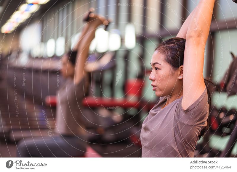 Ethnische Sportlerin beim Training mit Hanteln auf einer Bank in einem modernen Fitnessstudio Frau Kurzhantel Bizeps Steigung Übung Athlet Wohlbefinden sitzen