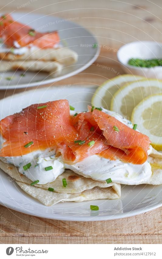 Portionen von leckerem Naan-Brot mit Lachs auf Tellern Fladenbrot Lebensmittel Sauerrahm grün Zwiebel Tisch geschmackvoll Speise Garnierung Saucen Filet hölzern