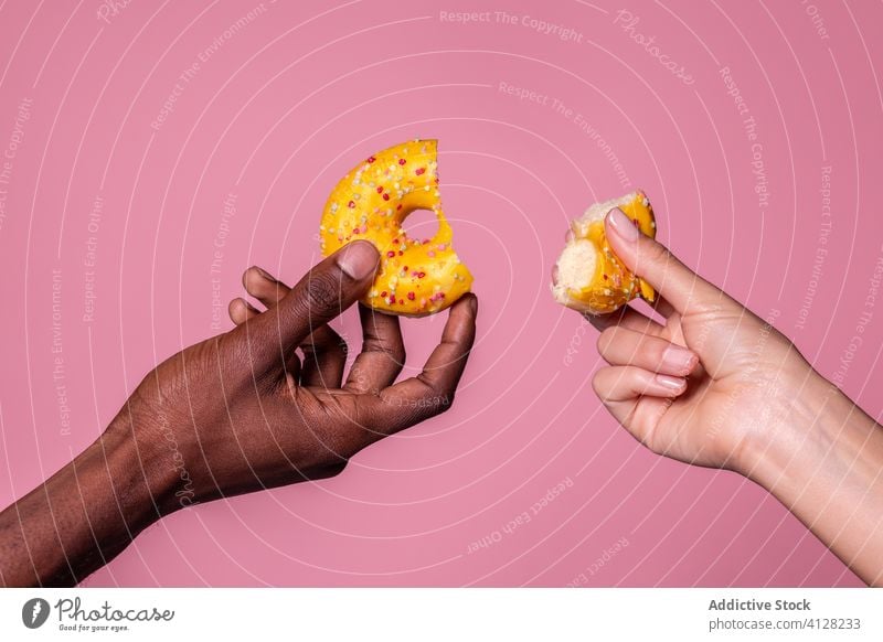 Crop multiracial Hände halten gebissen Donut auf rosa Hintergrund Doughnut süß Paar Hand geschmackvoll Lebensmittel lecker Halt Dessert Snack Gebäck Bäckerei