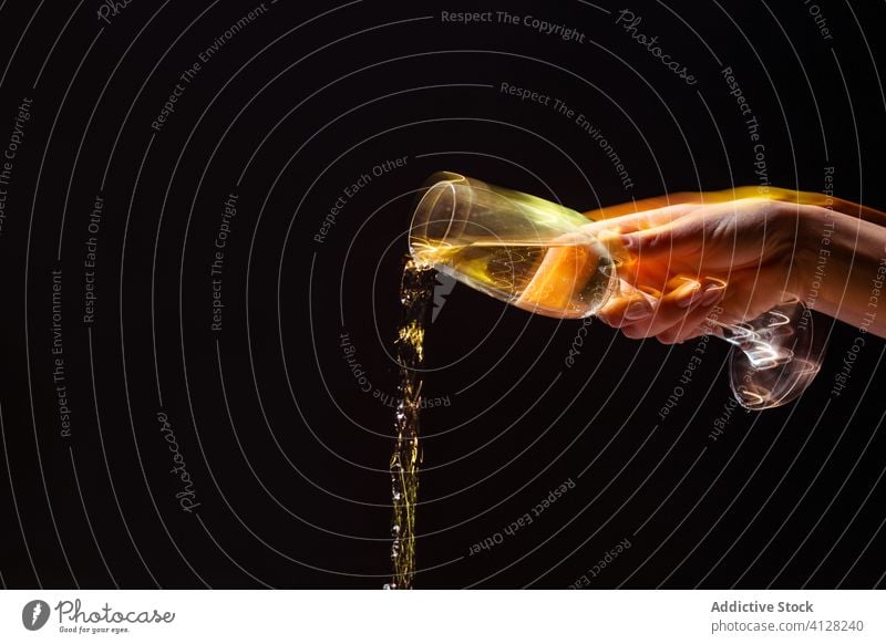 Crop anonyme Person gießt Getränk aus Glas auf schwarzem Hintergrund Hand Alkohol Halt Party trinken eingießen feiern Spaß Champagne Feiertag unterhalten frisch