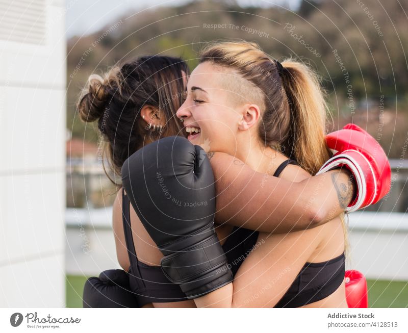 Fröhliche Boxerinnen in Handschuhen, die sich umarmen Frauen Umarmung Boxsport Training Kämpfer heiter Sport multiethnisch vielfältig rassenübergreifend Straße