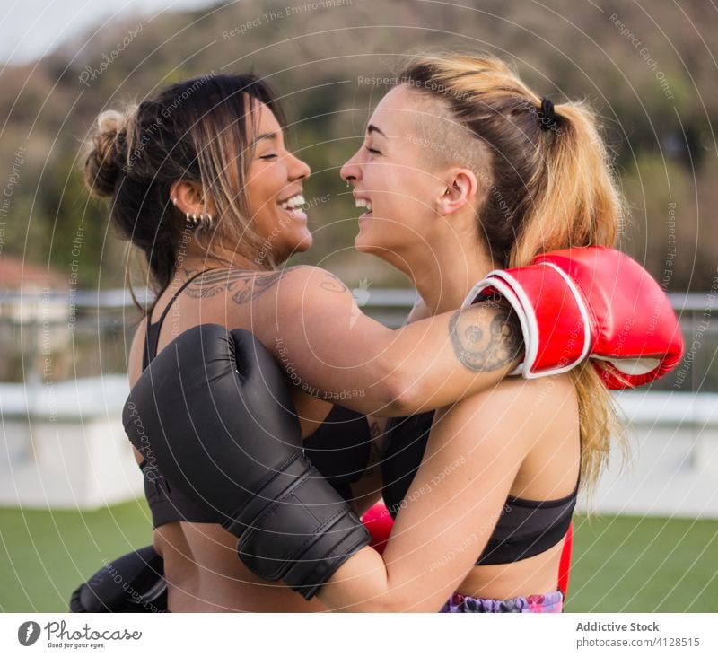 Fröhliche Boxerinnen in Handschuhen, die sich umarmen Frauen Umarmung Boxsport Training Kämpfer heiter Sport multiethnisch vielfältig rassenübergreifend Straße