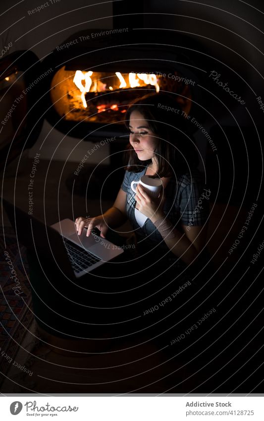 Frau mit Laptop im dunklen Wohnzimmer am Kamin Feuerstelle Browsen Kälte Wochenende Inhalt benutzend Netbook dunkel Lächeln heiter froh sitzen Stock Tasse