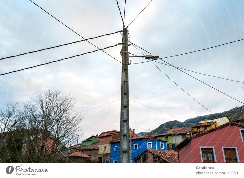 Straßenlaterne, Stromkabel, ein buntes Dorf, kahle Bäume an einem Wintermorgen. Straßenbeleuchtung Strommast Straßenlampe Energie Energieverteilung Himmel