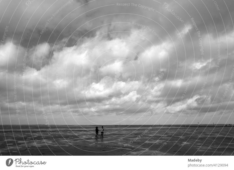 Dramatische Regenwolken im Herbst über dem Watt an der Küste der Nordsee in Bensersiel bei Esens in Ostfriesland in Niedersachsen, fotografiert in klassischem Schwarzweiß