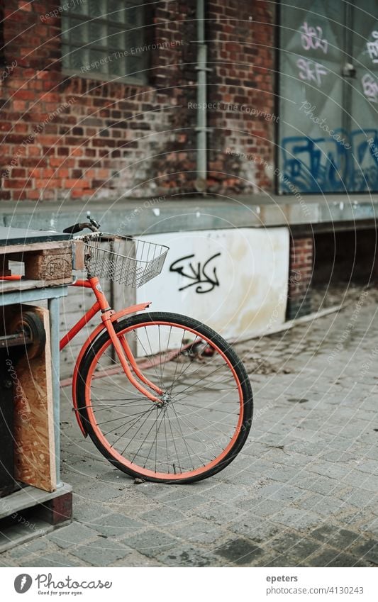 Orangefarbenes Fahrrad in einem industriellen Lagerhausviertel in Hamburg Deutschland Oberhafen Backsteinwand Arbeitsweg dreckig grau industrieller Stil orange