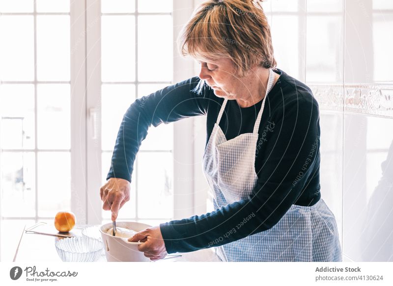 Ältere Frau macht Teig für Muffins in der Küche machen Teigwaren mischen Schürze Senior Bestandteil Bäckerei älter gealtert Koch Konditor stehen Tisch heimwärts