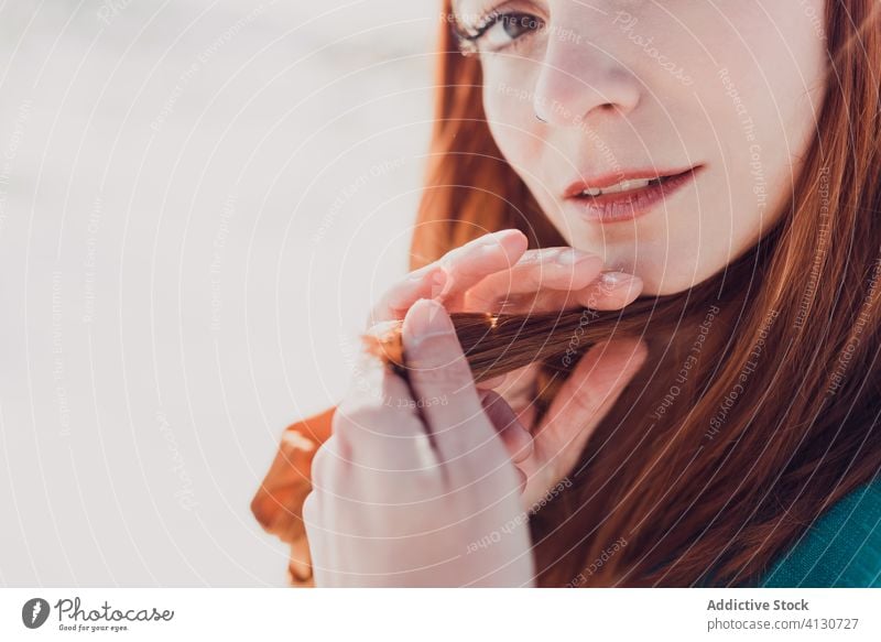 Junge schöne Frau mit langen roten Haaren in türkisfarbenem Outfit schaut in die Kamera, während sie in einem verschneiten Feld an einem sonnigen Tag steht Stil